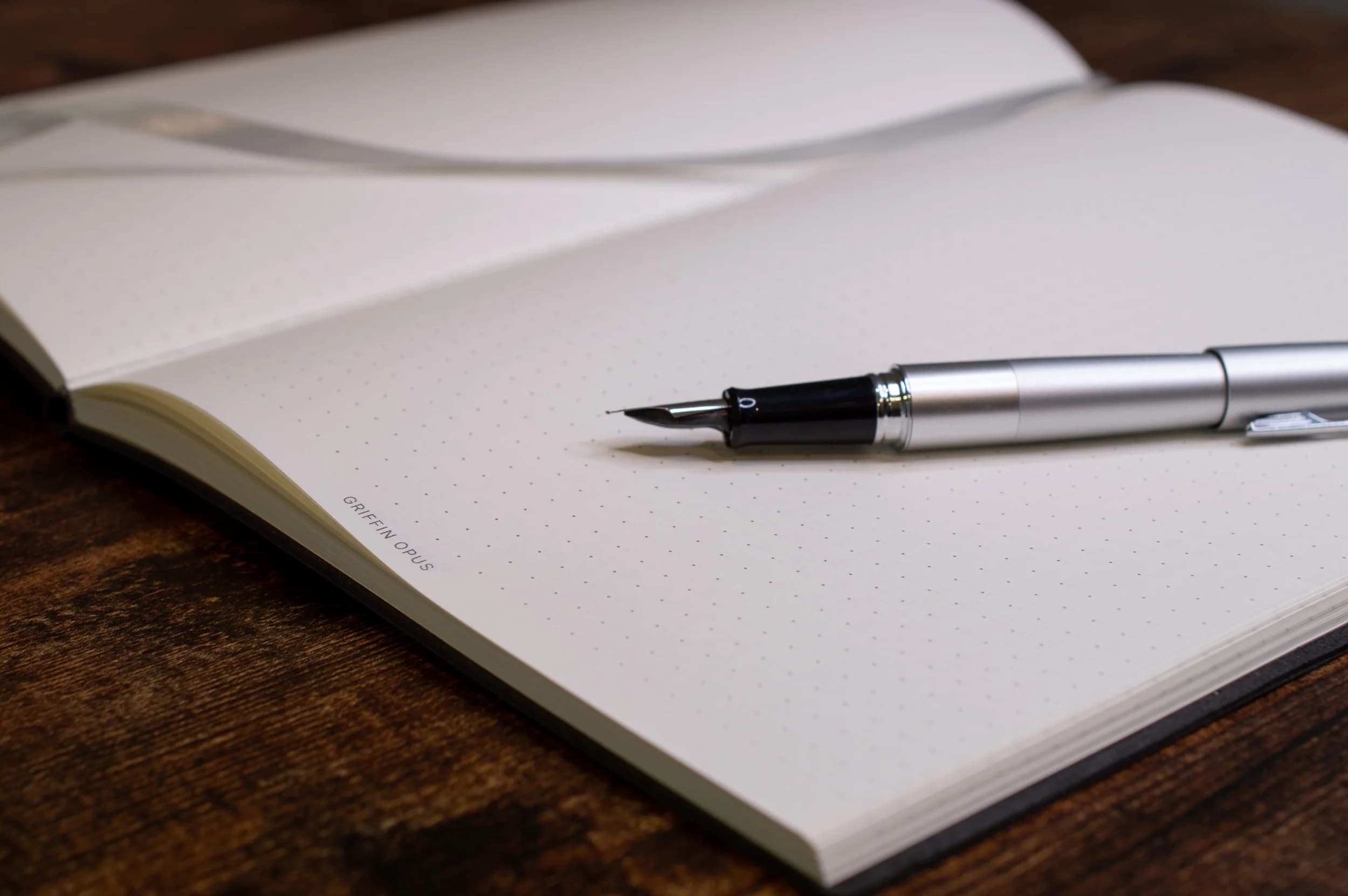 An open Griffin Opus Flexbound notebook with a fountain pen resting on the dot-grid page